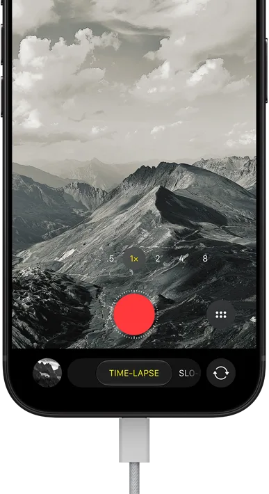 iPhone 18 Pro, face avant, affichant un paysage montagneux, avec le mode caméra incrusté en mode Accéléré, avec câble d’alimentation branché sur le port de charge