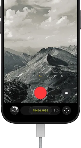 iPhone 18 Pro, face avant, affichant un paysage montagneux, avec le mode caméra incrusté en mode Accéléré, avec câble d’alimentation branché sur le port de charge